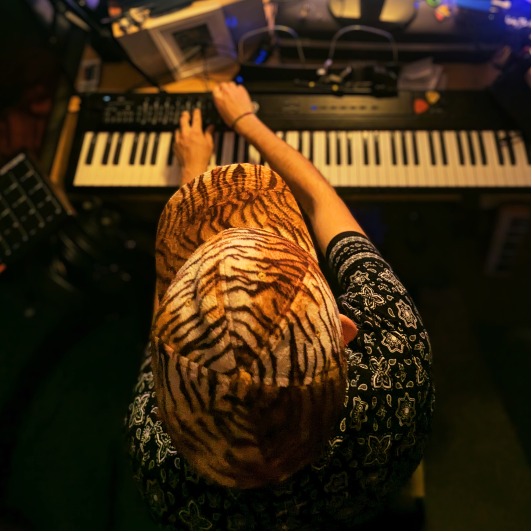 view from directly above of alexei playing a keyboard. his face is not visible, only the top of his leopard baseball cap.