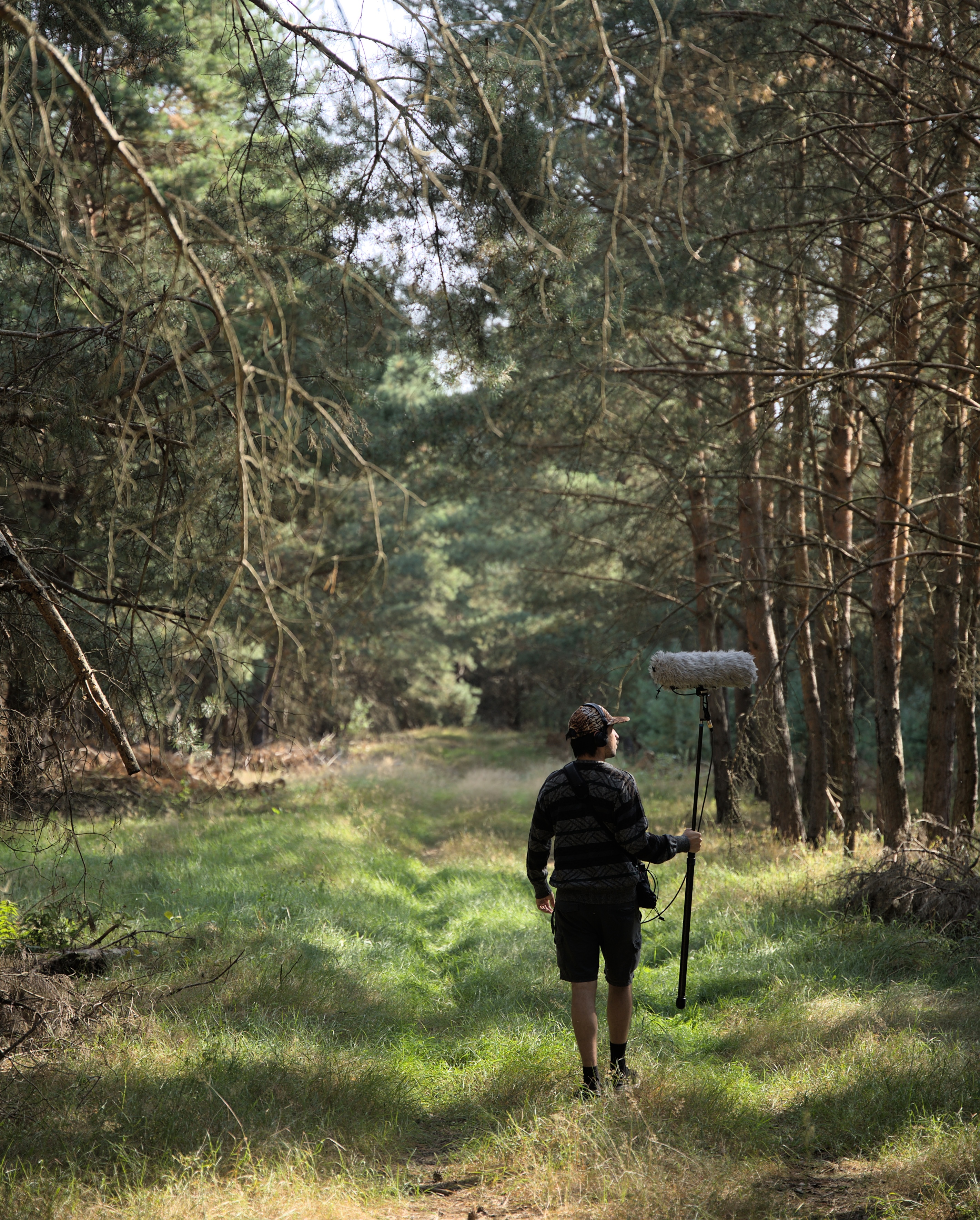 alexei walks in a forest, carrying a boom mic.